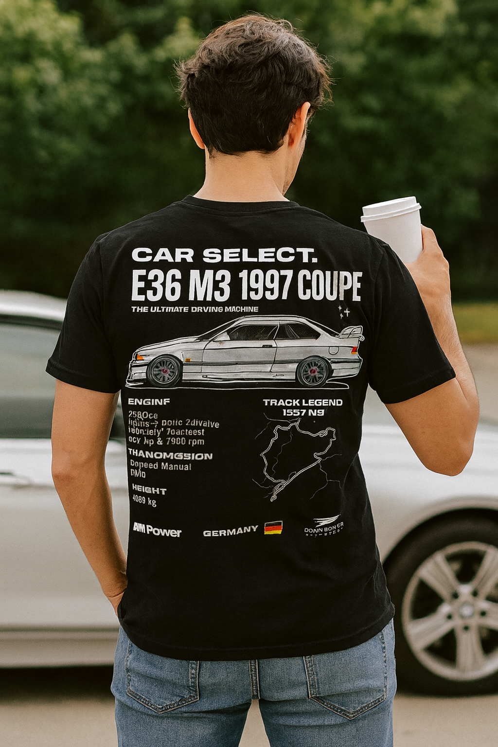 Person wearing a black t-shirt with car design and text, holding a coffee cup outdoors.