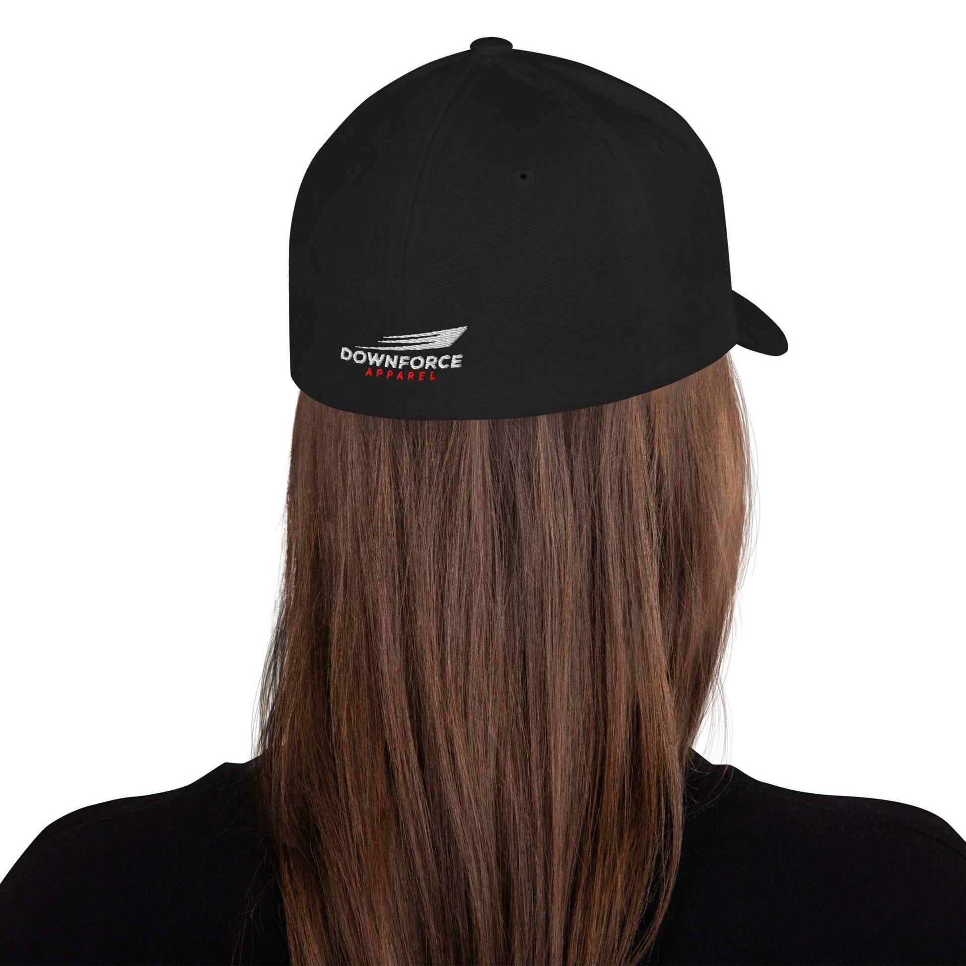 Black Downforce Apparel Flexfit cap with embroidered logo on back, worn on long brown hair from rear view.